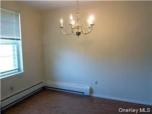 Unfurnished room with a baseboard radiator, dark wood-style floors, and a chandelier Unfurnished room with a baseboard radiator, dark wood-style floors, and a chandelier