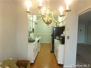 Kitchen featuring light countertops, wood finished floors, freestanding refrigerator, and white cabinetry Kitchen featuring light countertops, wood finished floors, freestanding refrigerator, and white cabinetry