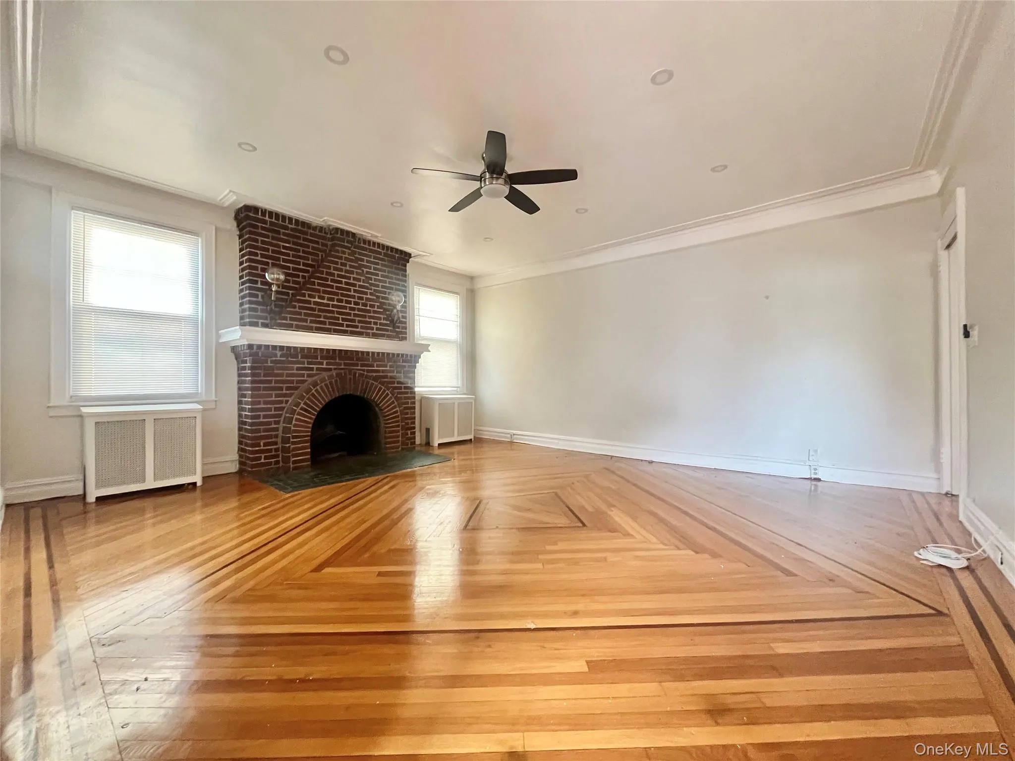 Unfurnished living room with radiator heating unit, crown molding, a brick fireplace, and a ceiling fan Unfurnished living room with radiator heating unit, crown molding, a brick fireplace, and a ceiling fan