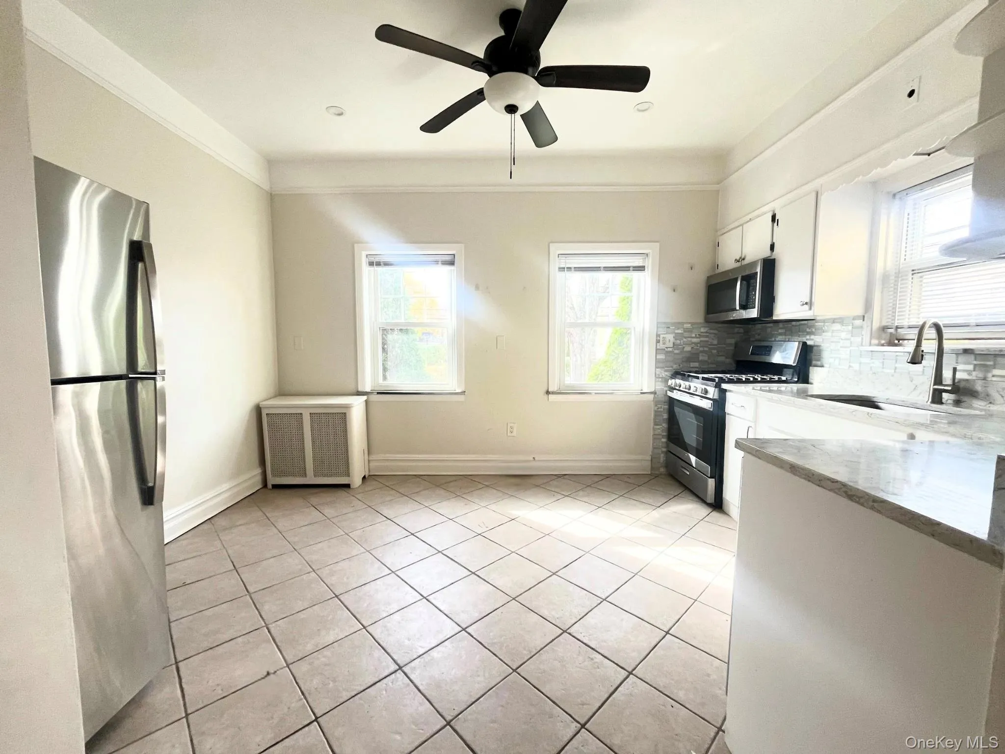 Kitchen with stainless steel appliances, light tile patterned floors, white cabinetry, light stone countertops, and radiator heating unit Kitchen with stainless steel appliances, light tile patterned floors, white cabinetry, light stone countertops, and radiator heating unit