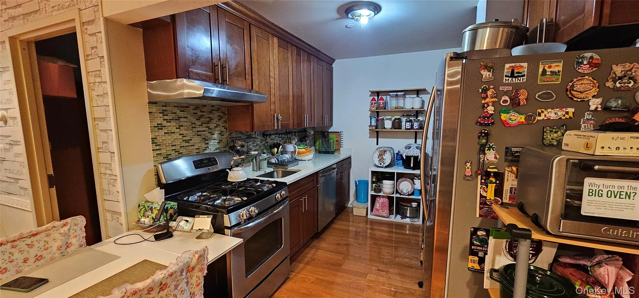 Kitchen featuring stainless steel appliances, tasteful backsplash, light wood-style floors, under cabinet range hood, and dark brown cabinetry Kitchen featuring stainless steel appliances, tasteful backsplash, light wood-style floors, under cabinet range hood, and dark brown cabinetry