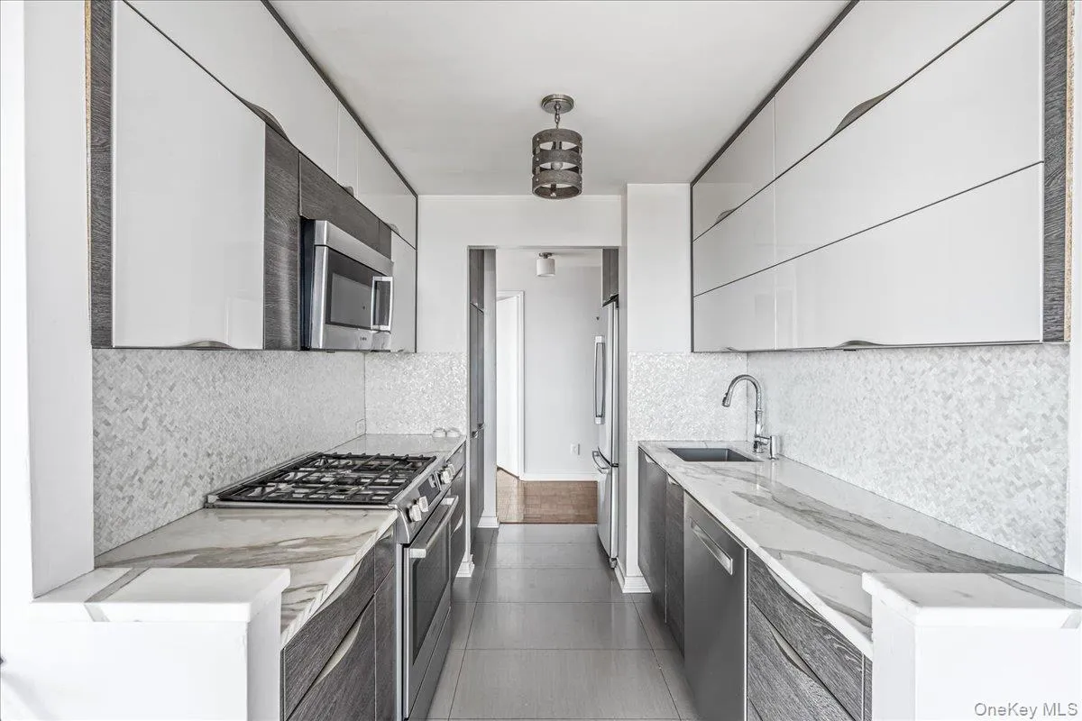 Kitchen with modern cabinets, appliances with stainless steel finishes, light stone countertops, and dark tile patterned flooring Kitchen with modern cabinets, appliances with stainless steel finishes, light stone countertops, and dark tile patterned flooring