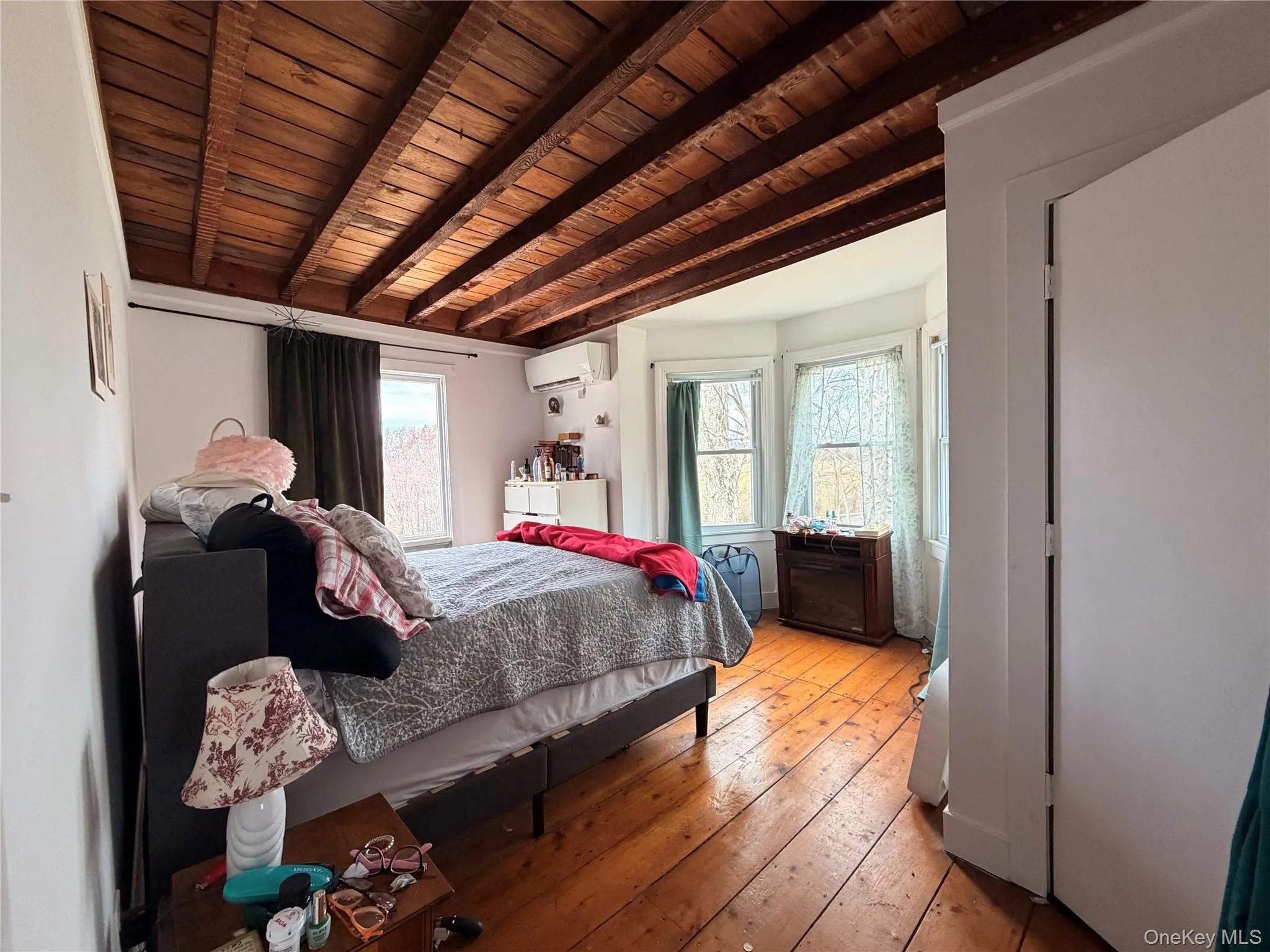 Bedroom 1 featuring hardwood flooring, a wood ceiling with exposed beams, multiple windows, and a mini split unit Bedroom 1 featuring hardwood flooring, a wood ceiling with exposed beams, multiple windows, and a mini split unit