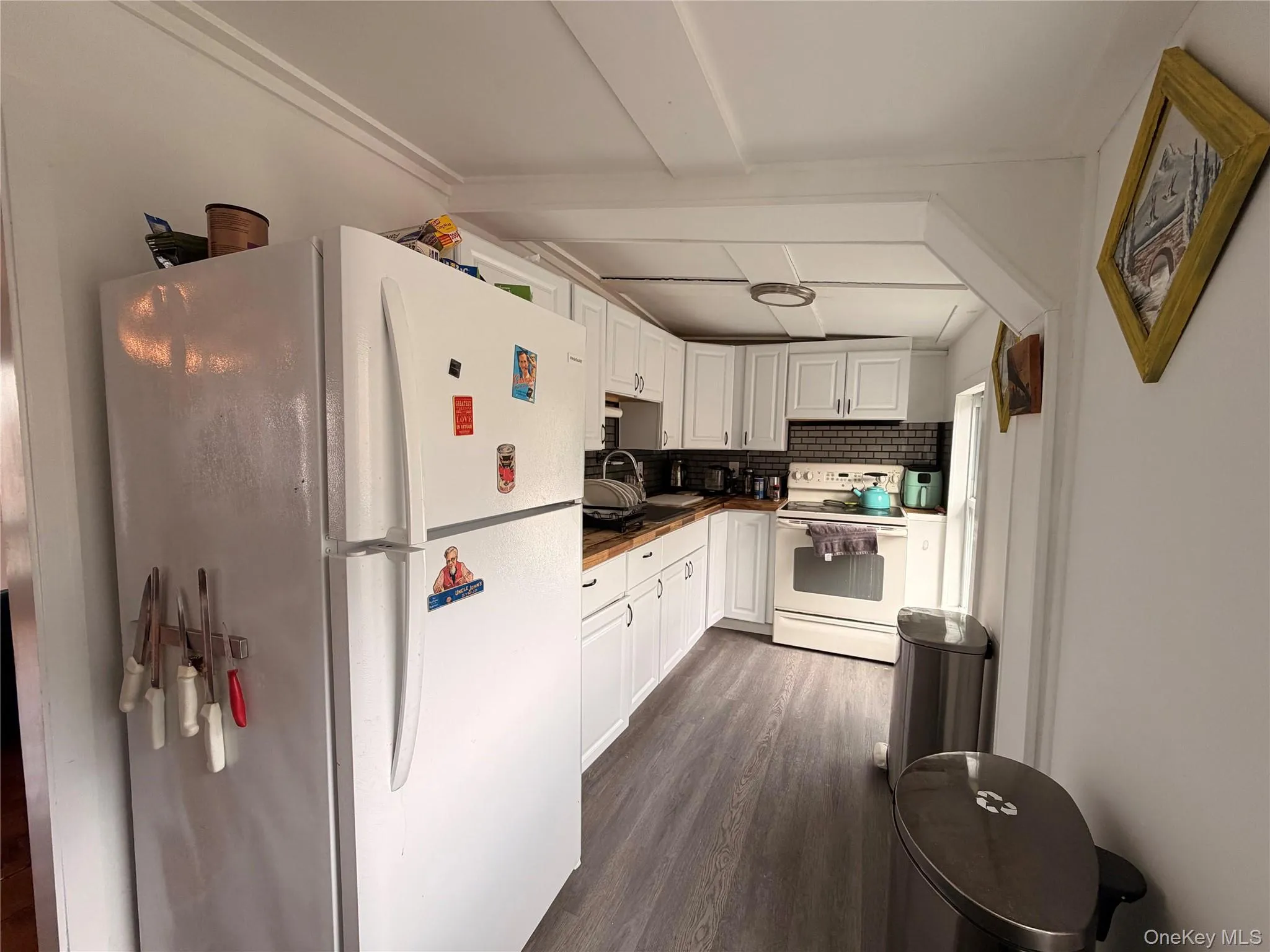 Kitchen featuring white appliances, white cabinetry, dark wood-style floors, and beam ceiling Kitchen featuring white appliances, white cabinetry, dark wood-style floors, and beam ceiling