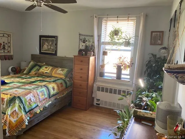 Bedroom featuring radiator heating unit, wood finished floors, and ceiling fan Bedroom featuring radiator heating unit, wood finished floors, and ceiling fan