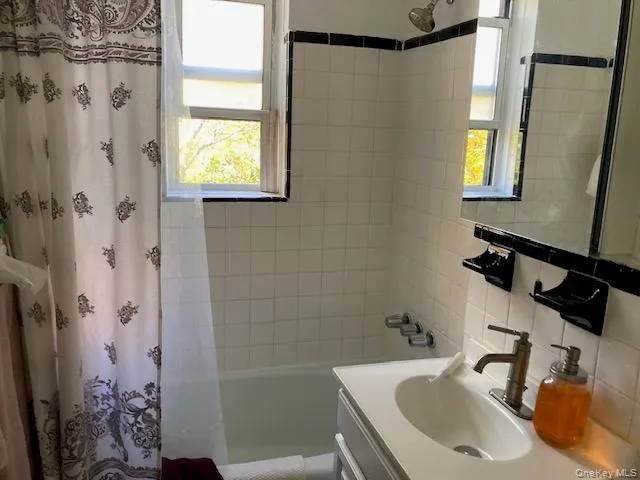 Bathroom featuring vanity, shower / bath combo, decorative backsplash, and tile walls Bathroom featuring vanity, shower / bath combo, decorative backsplash, and tile walls