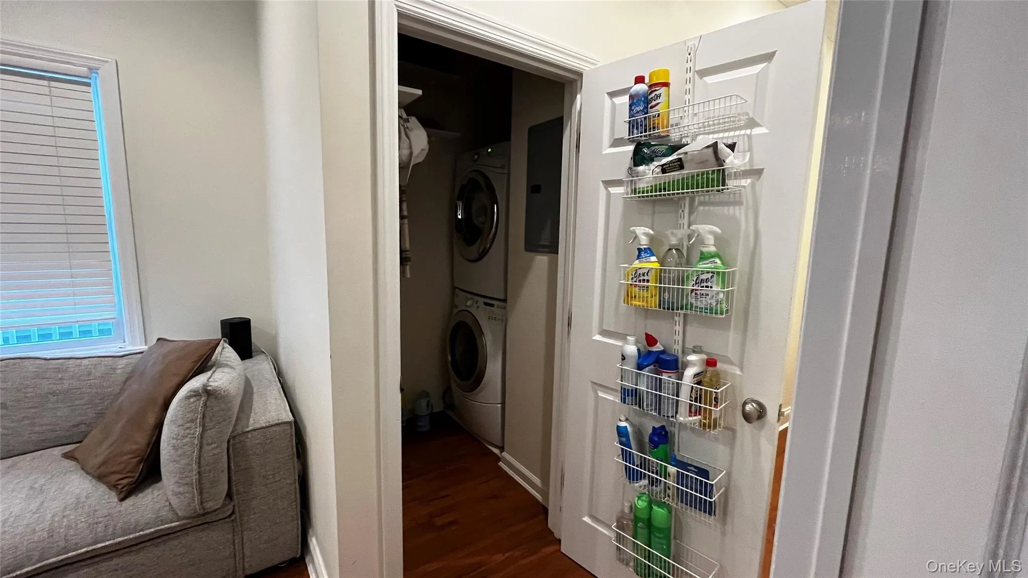 Laundry room with stacked washer and clothes dryer, dark wood finished floors, and electric panel Laundry room with stacked washer and clothes dryer, dark wood finished floors, and electric panel