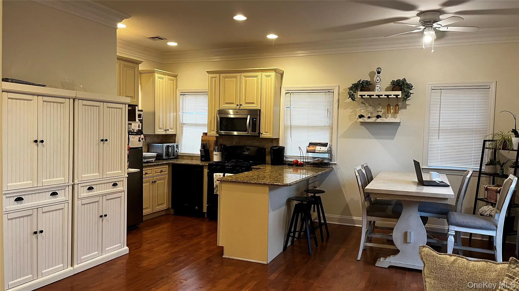 Kitchen featuring cream cabinets, ornamental molding, black appliances, dark wood finished floors, and a peninsula Kitchen featuring cream cabinets, ornamental molding, black appliances, dark wood finished floors, and a peninsula