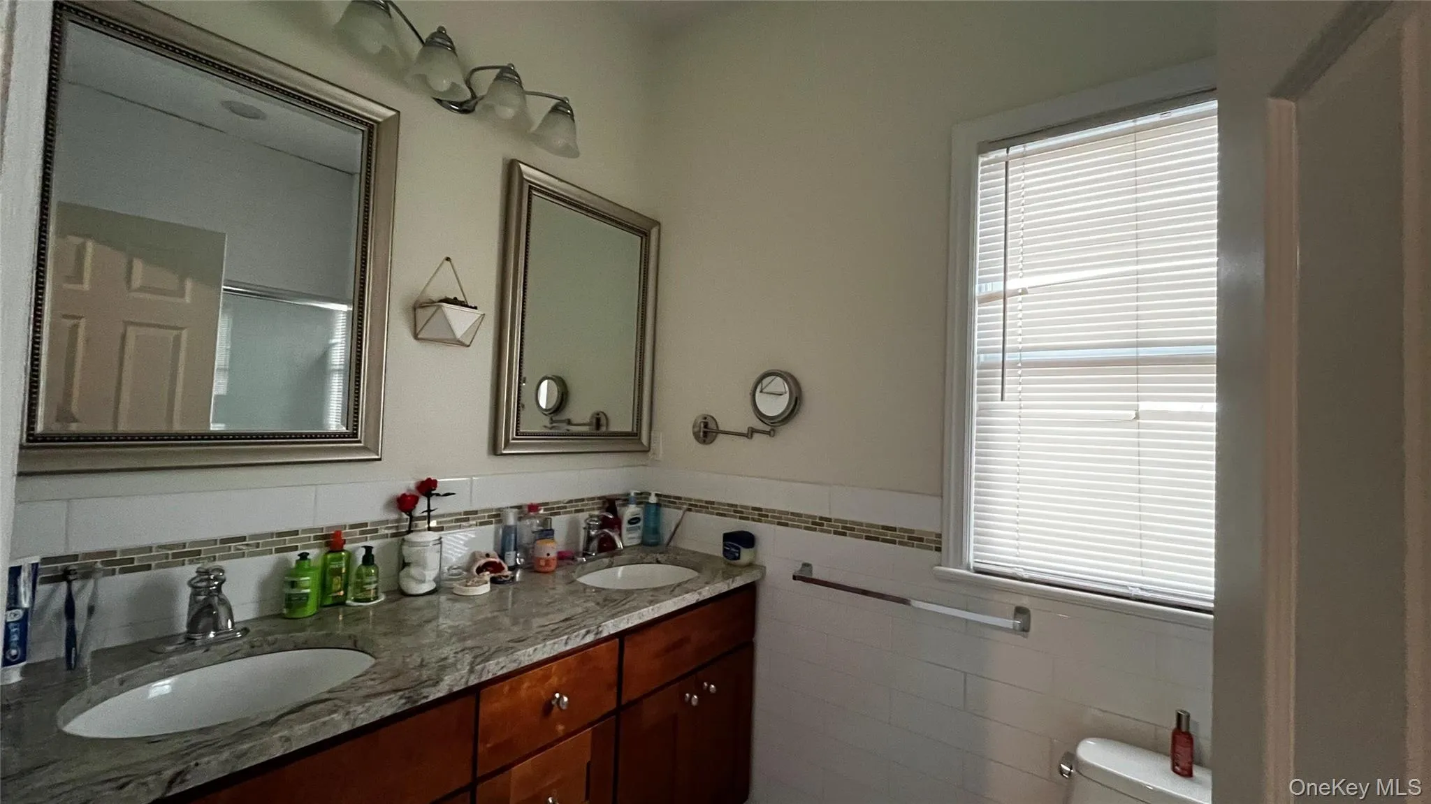 Bathroom featuring double vanity, healthy amount of natural light, tile walls, and a wainscoted wall Bathroom featuring double vanity, healthy amount of natural light, tile walls, and a wainscoted wall