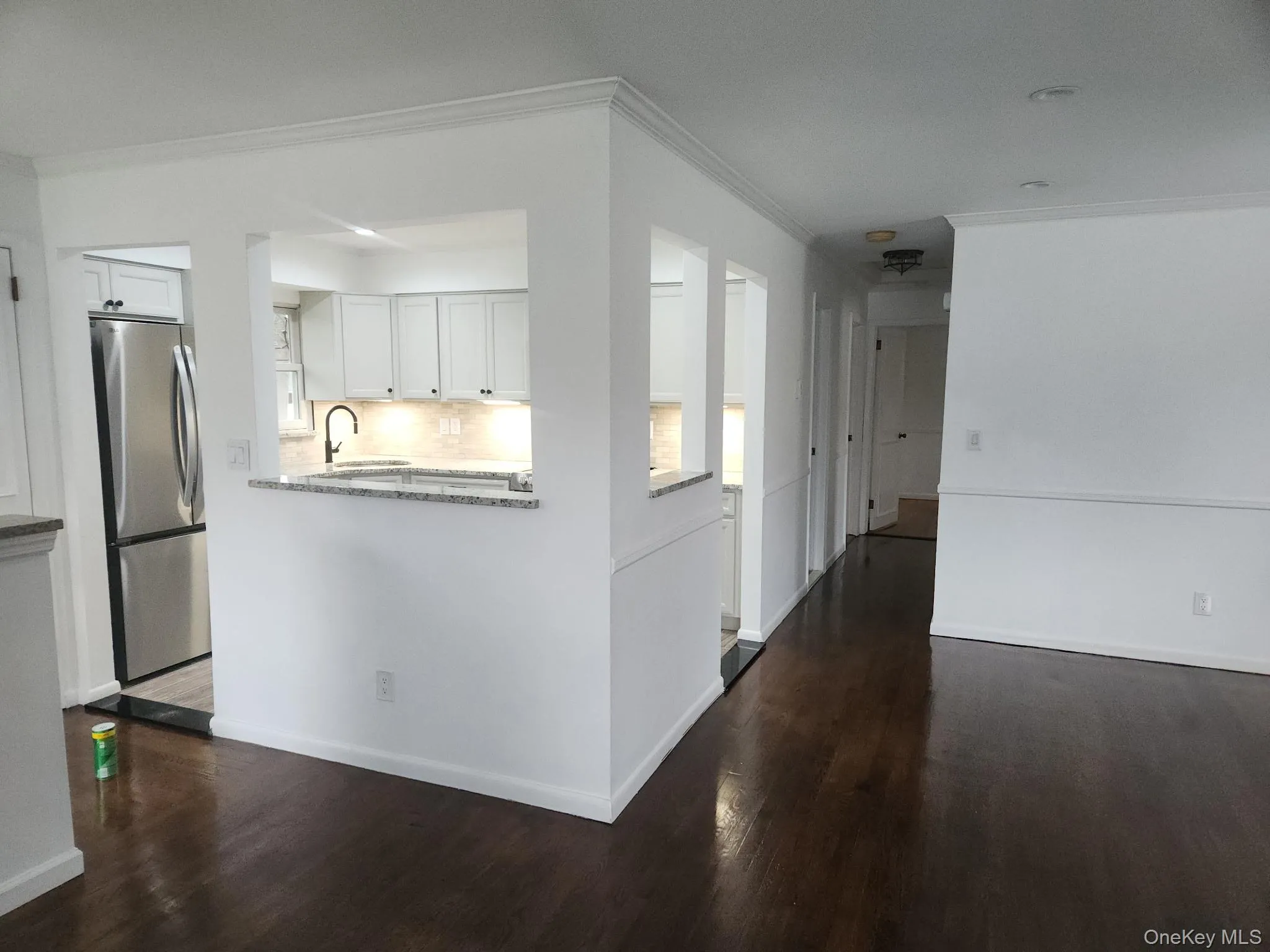 Kitchen with white cabinets, ornamental molding, dark wood finished floors, freestanding refrigerator, and light stone counters Kitchen with white cabinets, ornamental molding, dark wood finished floors, freestanding refrigerator, and light stone counters