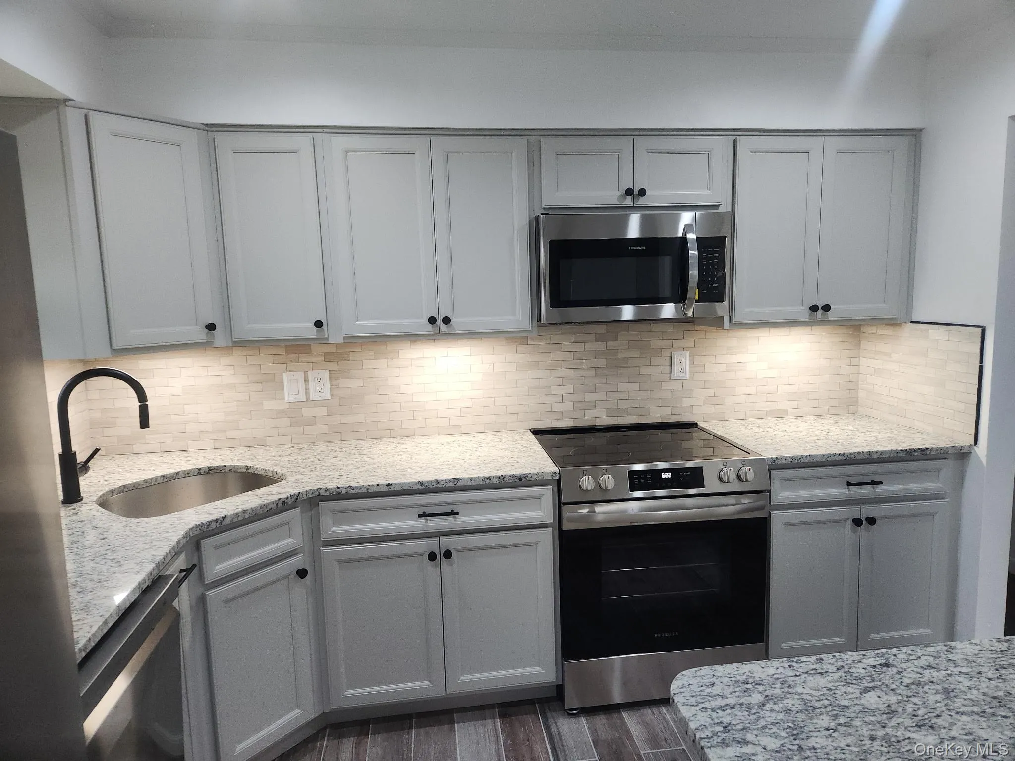 Kitchen with appliances with stainless steel finishes, light stone countertops, gray cabinetry, and backsplash Kitchen with appliances with stainless steel finishes, light stone countertops, gray cabinetry, and backsplash