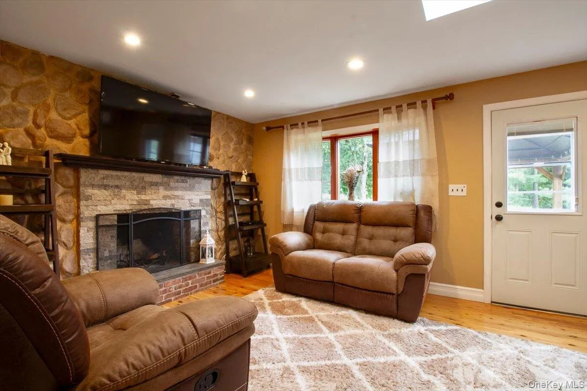 Living room featuring wood finished floors, a stone fireplace, and recessed lighting Living room featuring wood finished floors, a stone fireplace, and recessed lighting