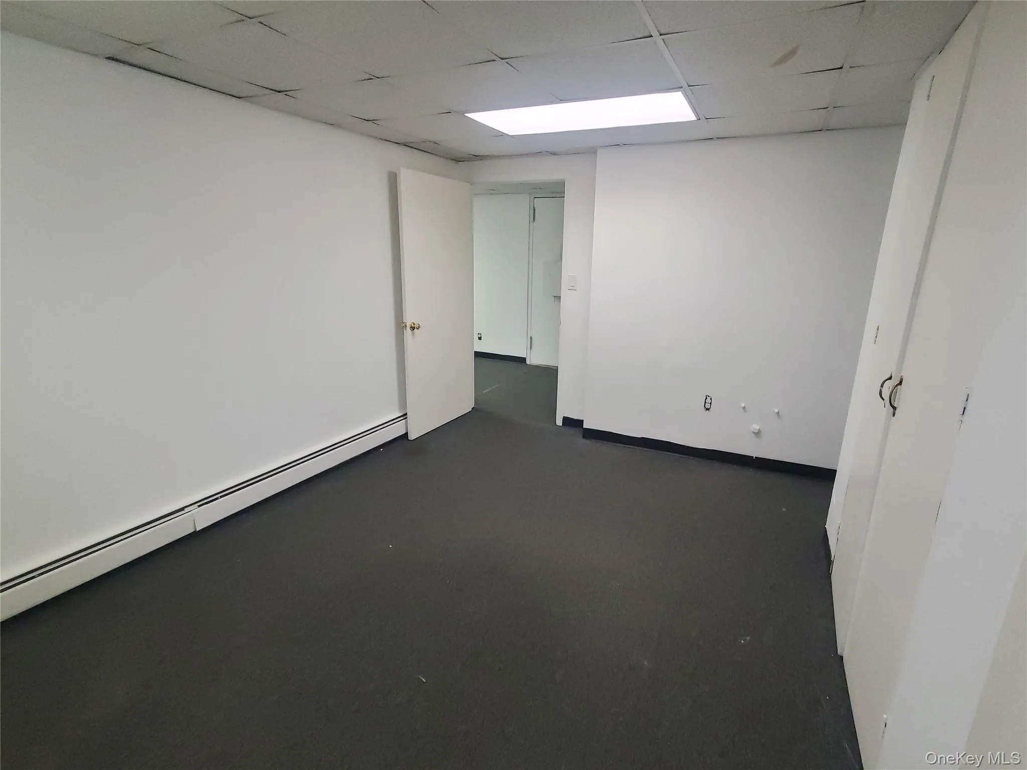 Private office area with a drop ceiling, a baseboard radiator, and dark colored carpet Private office area with a drop ceiling, a baseboard radiator, and dark colored carpet