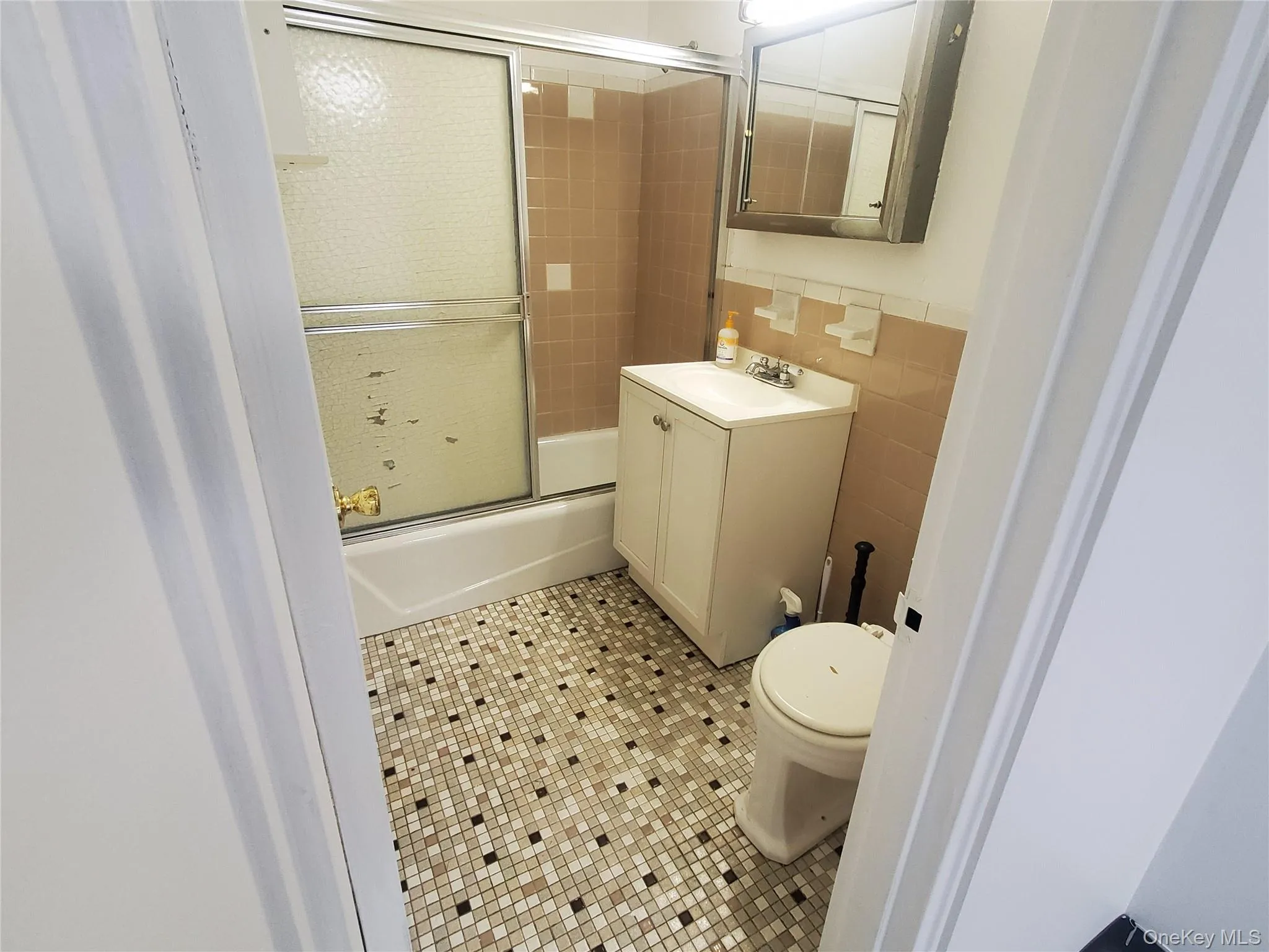Full bathroom with tile walls, vanity, enclosed tub / shower combo, light tile patterned floors, and a wainscoted wall Full bathroom with tile walls, vanity, enclosed tub / shower combo, light tile patterned floors, and a wainscoted wall