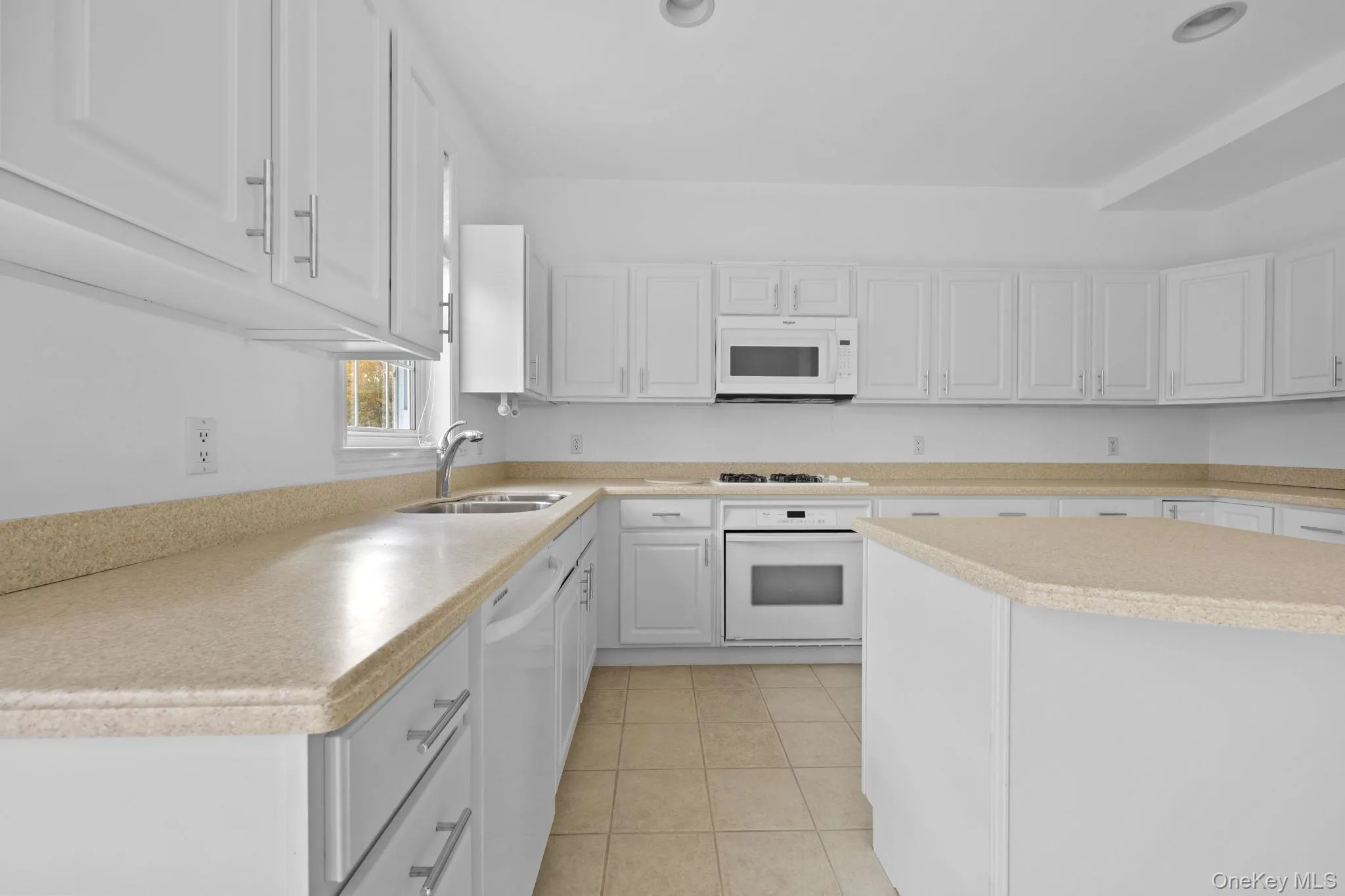 Kitchen with white cabinets, light countertops, light tile patterned floors, white appliances, and a kitchen island Kitchen with white cabinets, light countertops, light tile patterned floors, white appliances, and a kitchen island