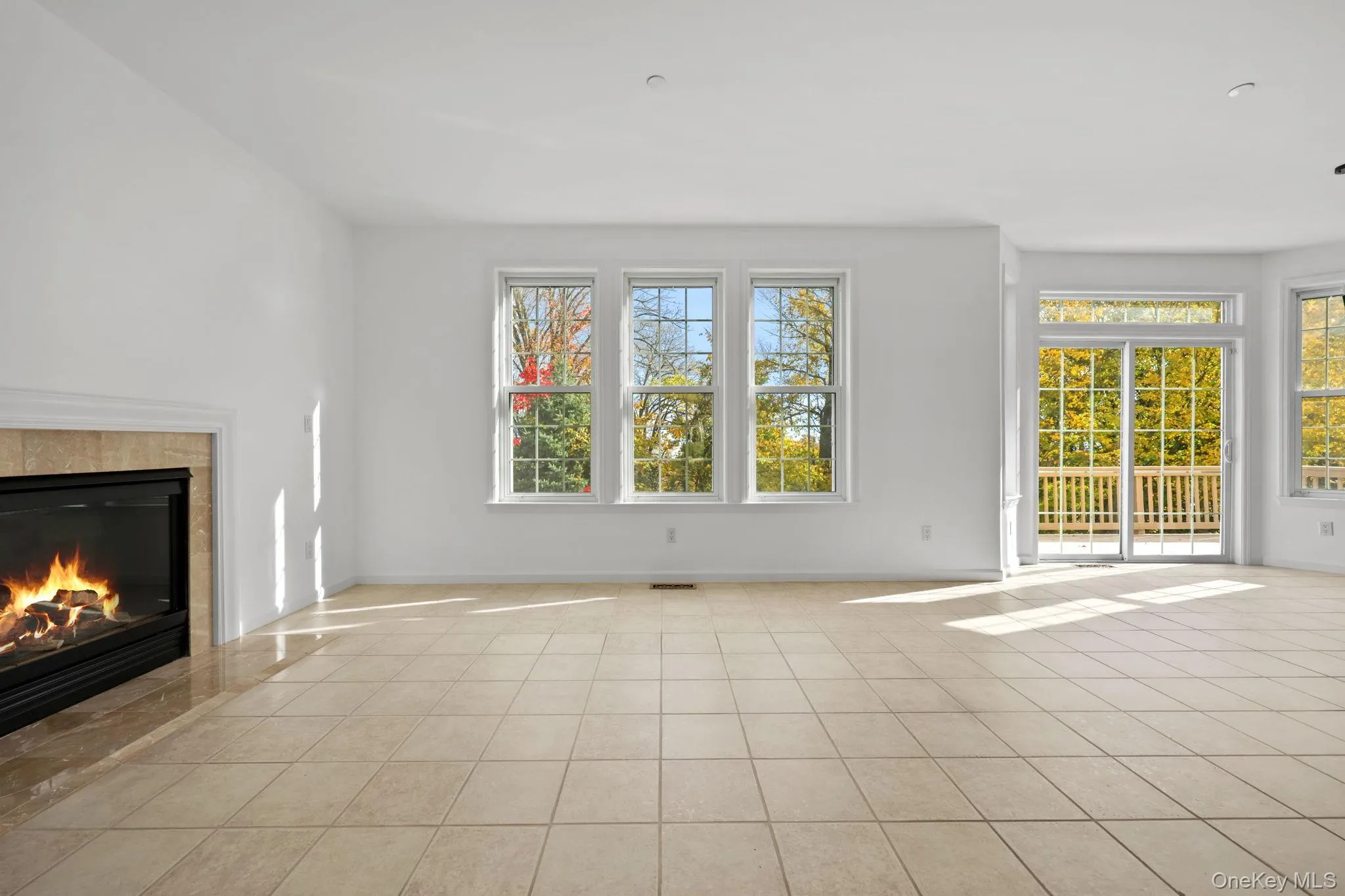 Unfurnished living room featuring a fireplace, healthy amount of natural light, and light tile patterned floors Unfurnished living room featuring a fireplace, healthy amount of natural light, and light tile patterned floors