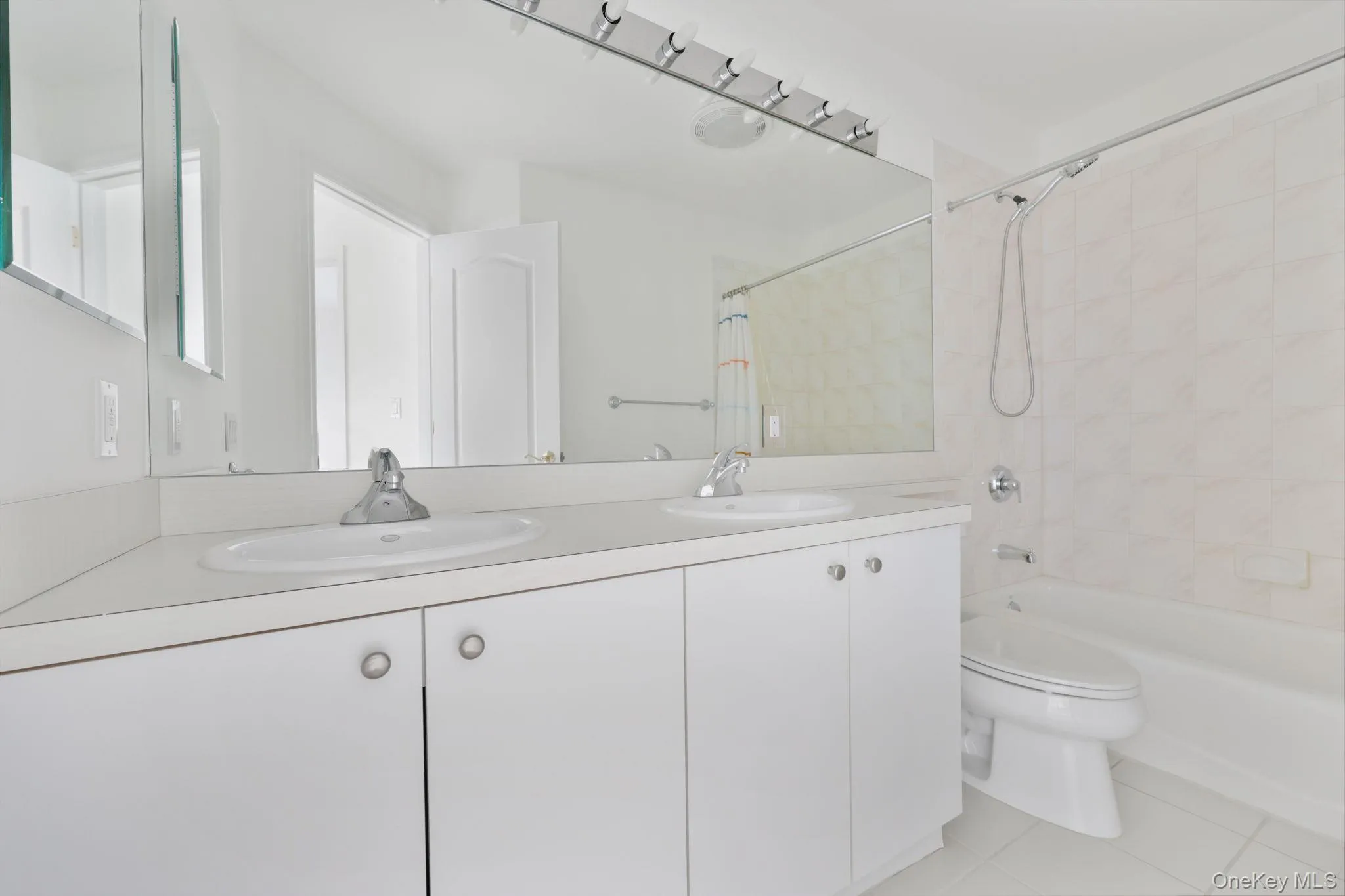 Bathroom with double vanity, light tile patterned floors, and shower / bath combo Bathroom with double vanity, light tile patterned floors, and shower / bath combo