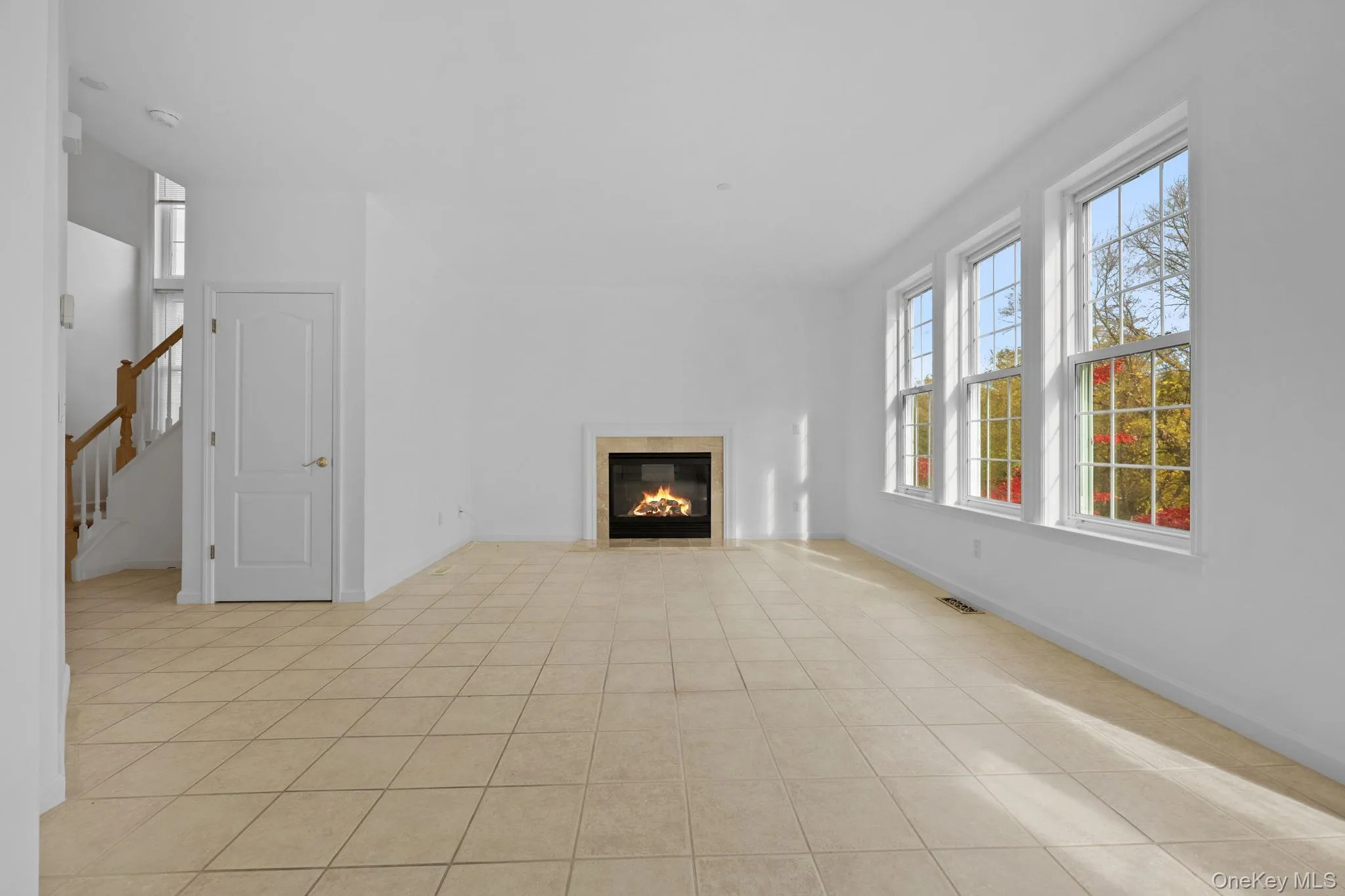 Unfurnished living room featuring a fireplace, healthy amount of natural light, light tile patterned flooring, and stairway Unfurnished living room featuring a fireplace, healthy amount of natural light, light tile patterned flooring, and stairway