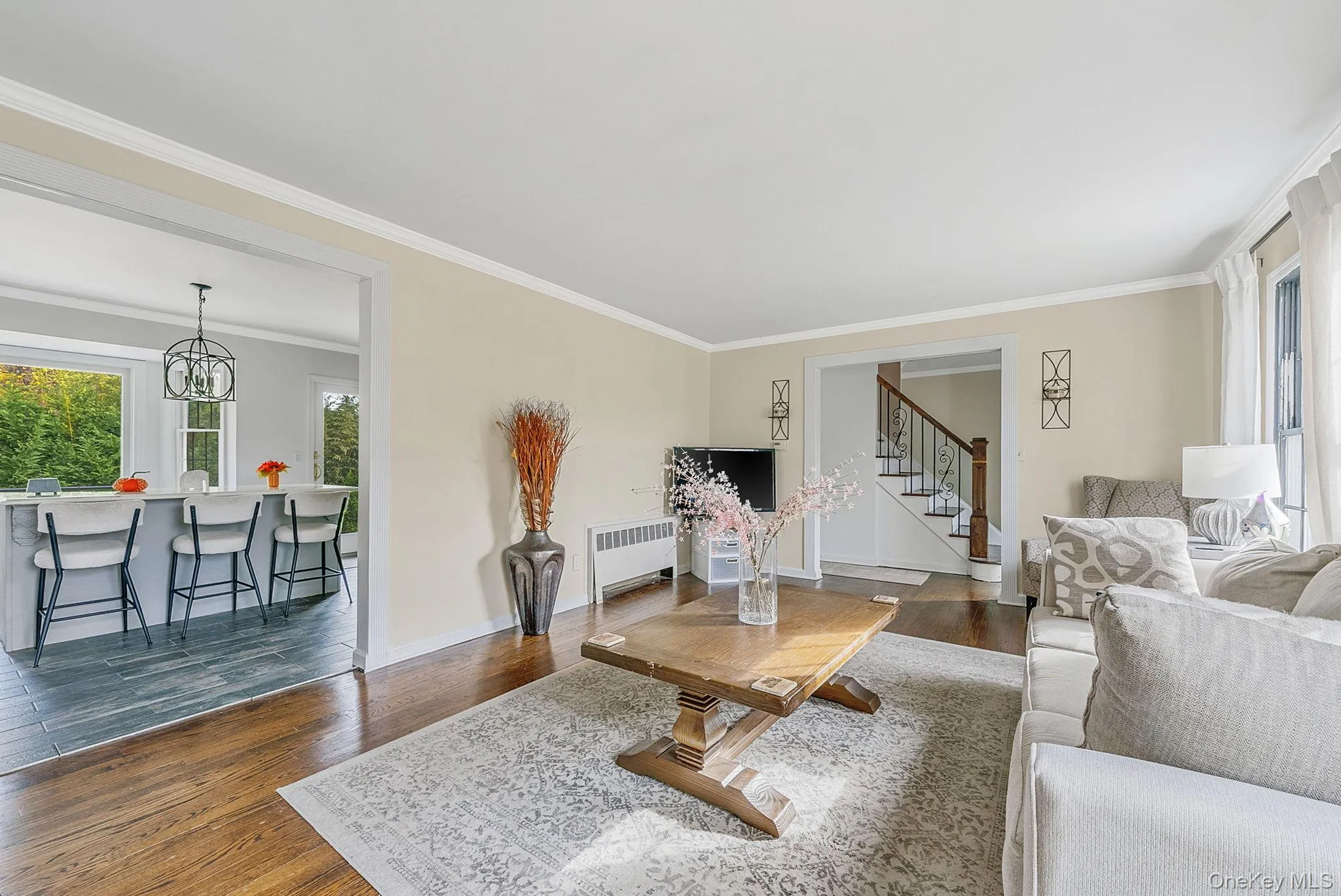 Living area featuring crown molding, dark wood-type flooring, radiator heating unit, a chandelier, and stairway Living area featuring crown molding, dark wood-type flooring, radiator heating unit, a chandelier, and stairway