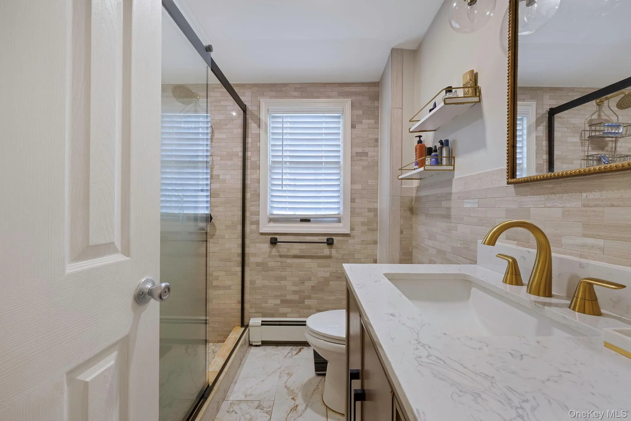 Bathroom featuring a shower stall, vanity, tile walls, baseboard heating, and light marble finish flooring Bathroom featuring a shower stall, vanity, tile walls, baseboard heating, and light marble finish flooring