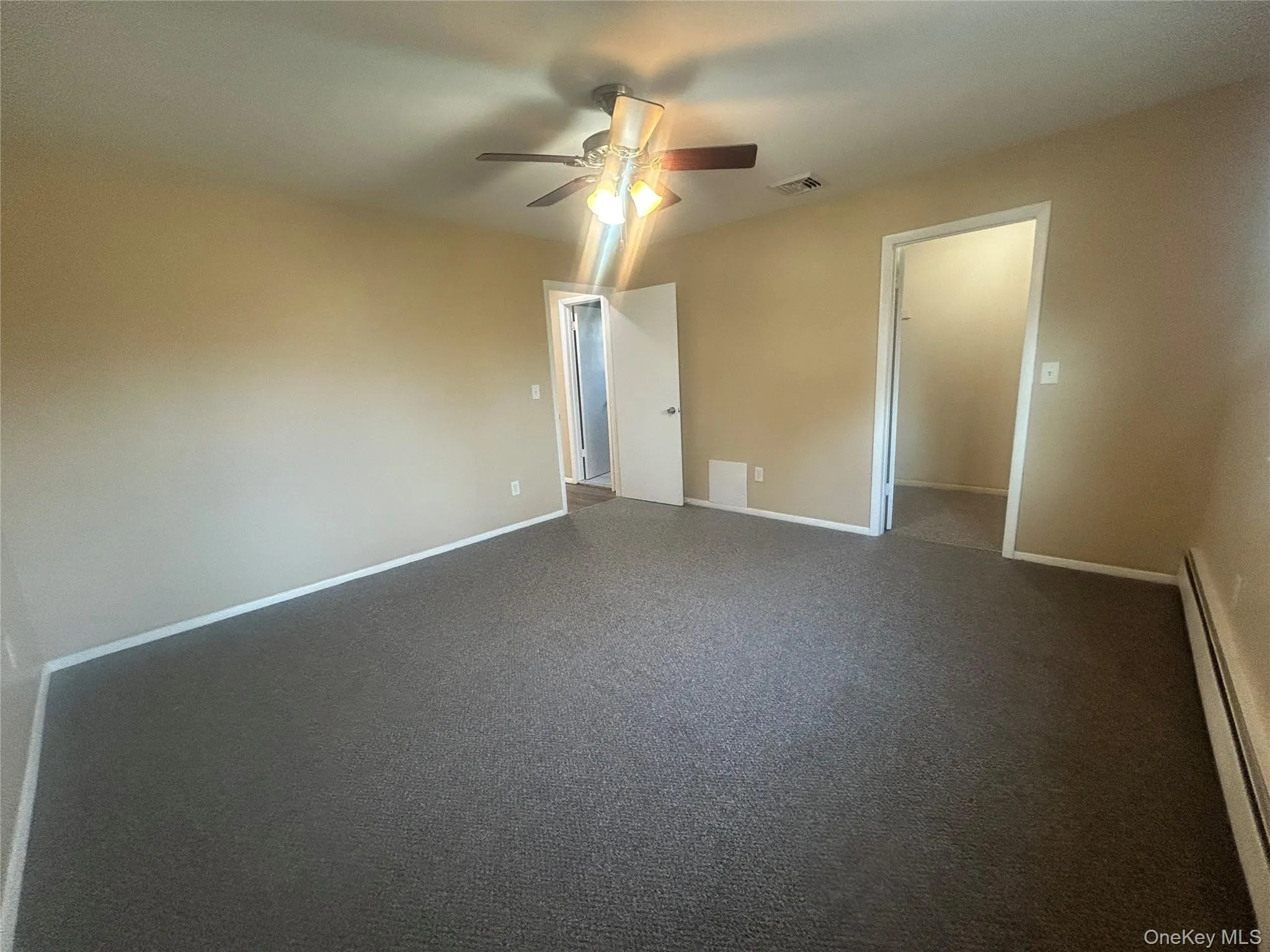 Unfurnished bedroom with a baseboard heating unit, ceiling fan, and dark carpet Unfurnished bedroom with a baseboard heating unit, ceiling fan, and dark carpet