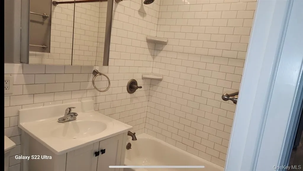 Bathroom with vanity, shower / bathtub combination, tile walls, and decorative backsplash Bathroom with vanity, shower / bathtub combination, tile walls, and decorative backsplash