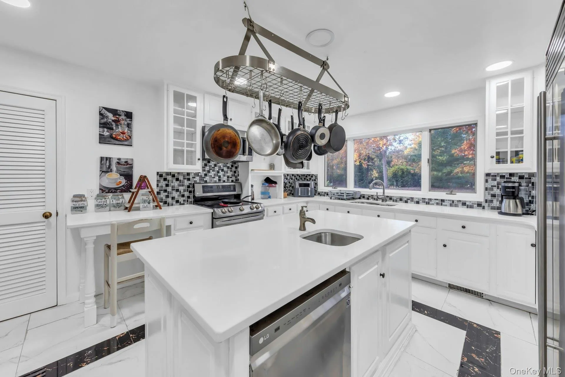 Kitchen with glass insert cabinets, white cabinets, recessed lighting, an island with sink, and light marble finish floors Kitchen with glass insert cabinets, white cabinets, recessed lighting, an island with sink, and light marble finish floors