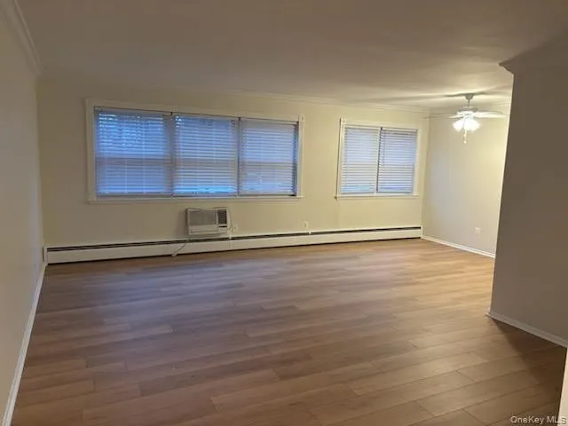 Empty room featuring light wood-type flooring, an AC wall unit, ceiling fan, a baseboard heating unit, and crown molding Empty room featuring light wood-type flooring, an AC wall unit, ceiling fan, a baseboard heating unit, and crown molding