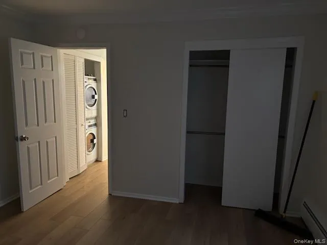 Unfurnished bedroom featuring baseboard heating, crown molding, a closet, stacked washing machine and dryer, and light wood-style floors Unfurnished bedroom featuring baseboard heating, crown molding, a closet, stacked washing machine and dryer, and light wood-style floors