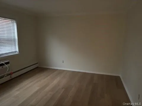 Unfurnished room featuring crown molding, light wood-style flooring, a baseboard radiator, and a wall unit AC Unfurnished room featuring crown molding, light wood-style flooring, a baseboard radiator, and a wall unit AC