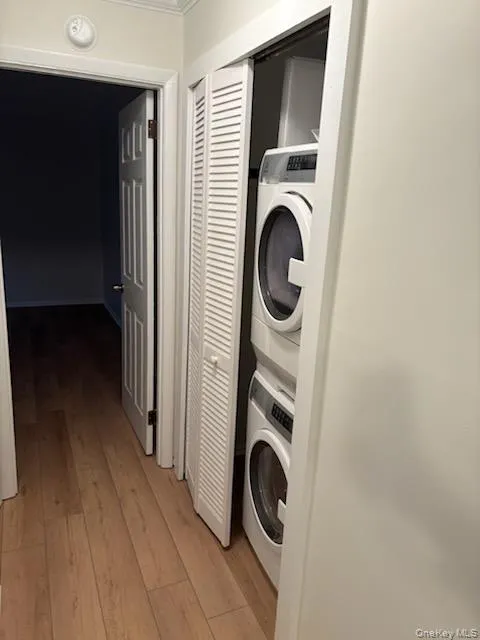 Washroom with light wood finished floors and stacked washer and clothes dryer Washroom with light wood finished floors and stacked washer and clothes dryer