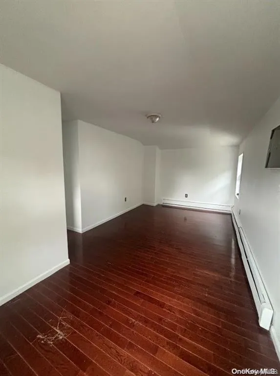 Unfurnished room featuring a baseboard radiator and dark wood-style floors Unfurnished room featuring a baseboard radiator and dark wood-style floors