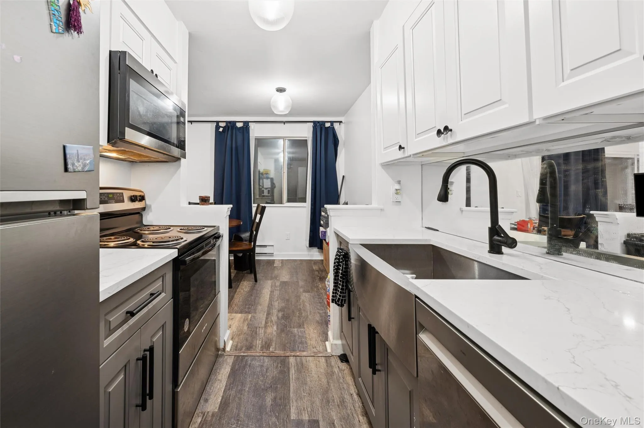 Kitchen with stainless steel appliances, dark wood-style flooring, light stone counters, white cabinetry, and a baseboard heating unit Kitchen with stainless steel appliances, dark wood-style flooring, light stone counters, white cabinetry, and a baseboard heating unit