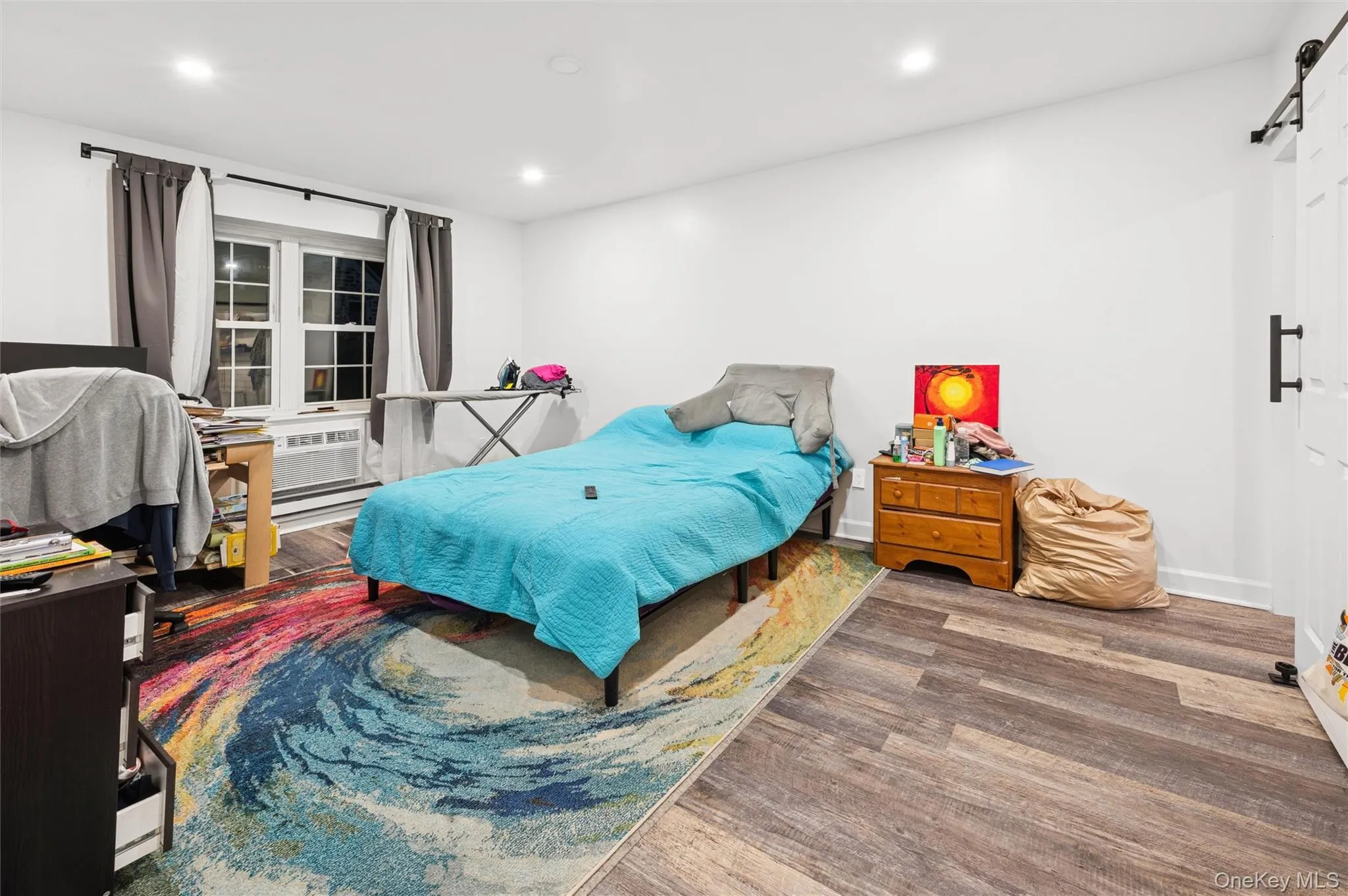 Bedroom with a barn door, recessed lighting, wood finished floors, and baseboard heating Bedroom with a barn door, recessed lighting, wood finished floors, and baseboard heating