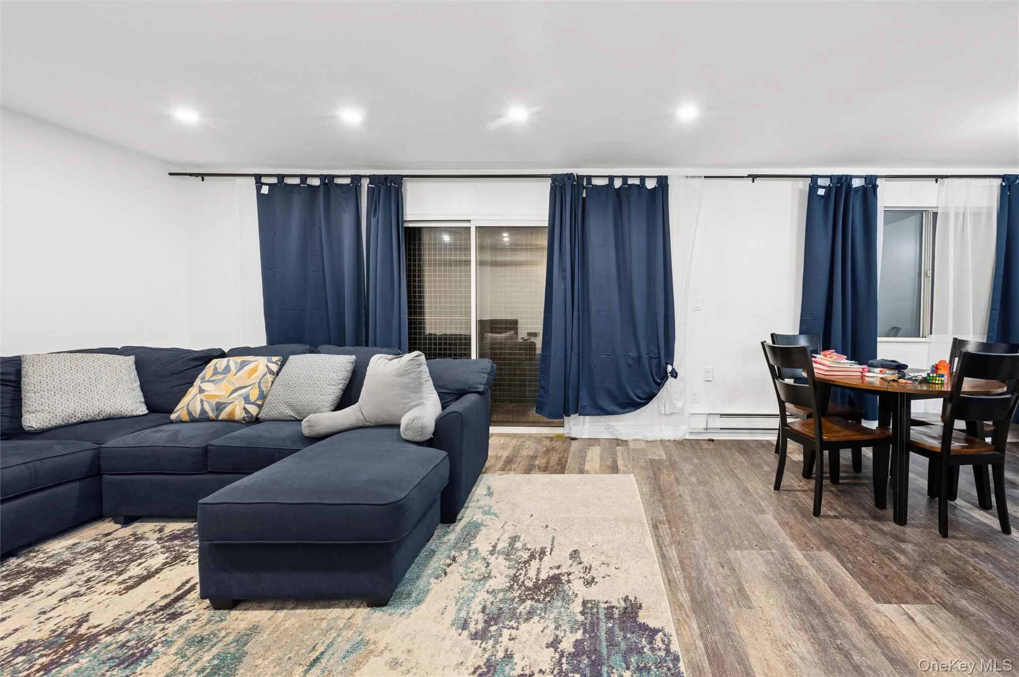 Living room with wood finished floors, recessed lighting, and a baseboard radiator Living room with wood finished floors, recessed lighting, and a baseboard radiator