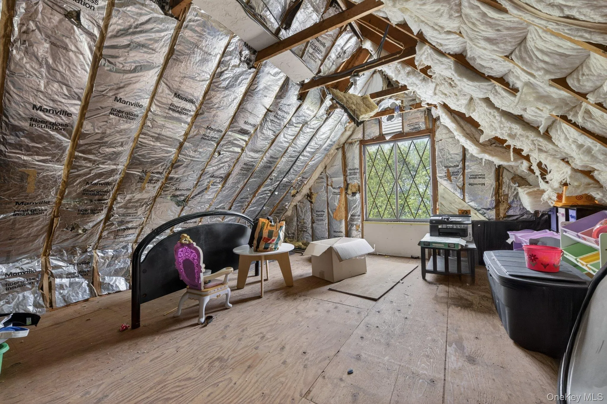 Attic space featuring exposed wood framing, foil-faced insulation, a diamond-pane window, and plywood subflooring Attic space featuring exposed wood framing, foil-faced insulation, a diamond-pane window, and plywood subflooring