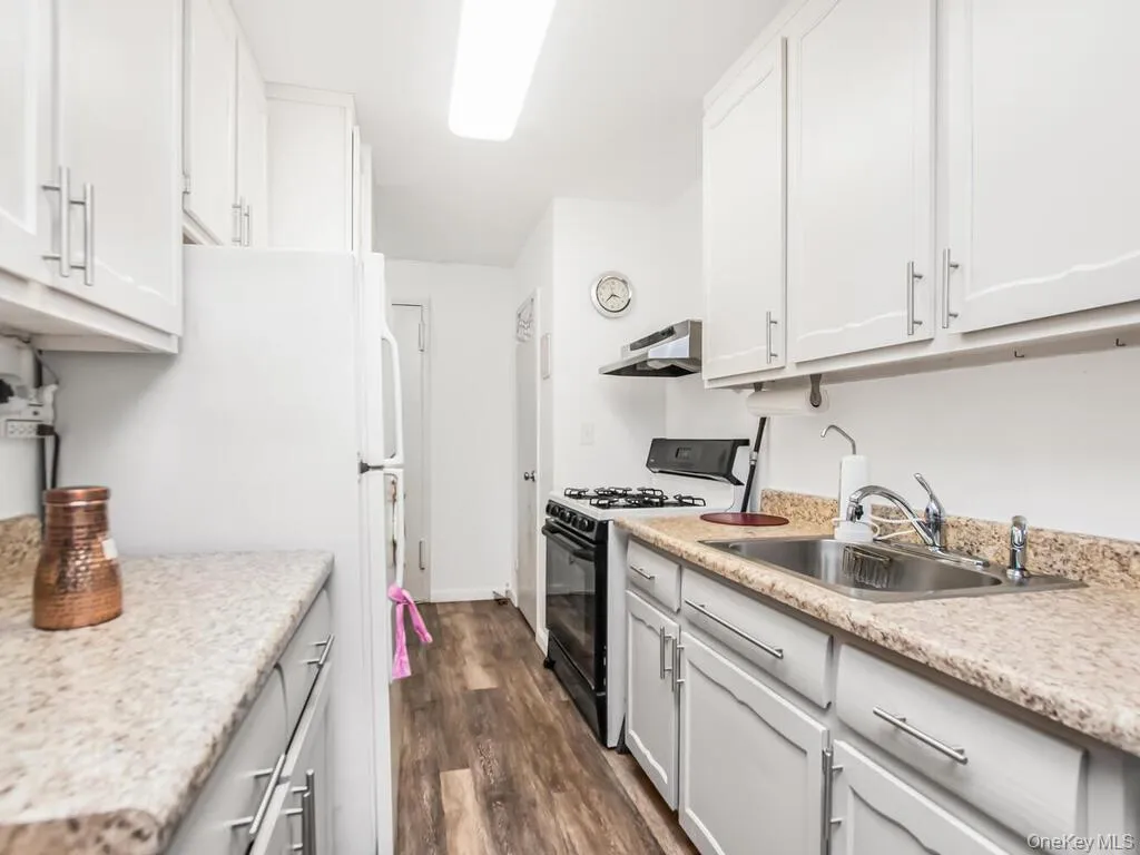 Kitchen featuring range with gas cooktop, dark wood-style flooring, range hood, freestanding refrigerator, and white cabinetry Kitchen featuring range with gas cooktop, dark wood-style flooring, range hood, freestanding refrigerator, and white cabinetry