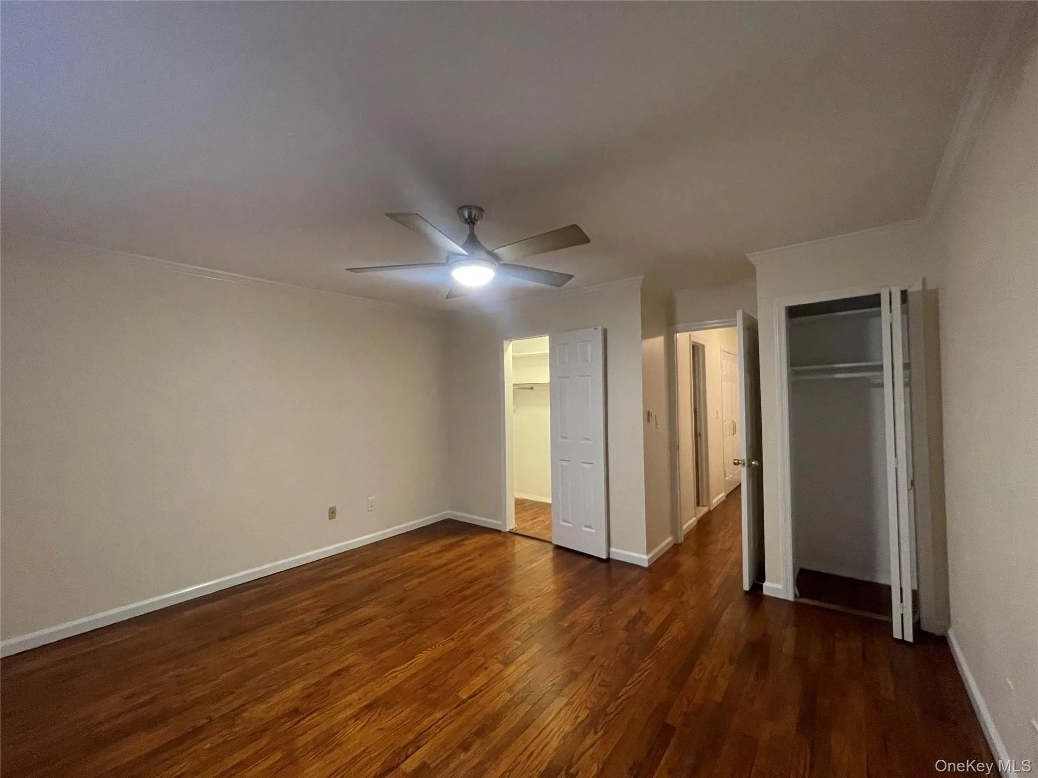 Unfurnished bedroom with dark wood-style flooring, ceiling fan, multiple closets, and crown molding Unfurnished bedroom with dark wood-style flooring, ceiling fan, multiple closets, and crown molding