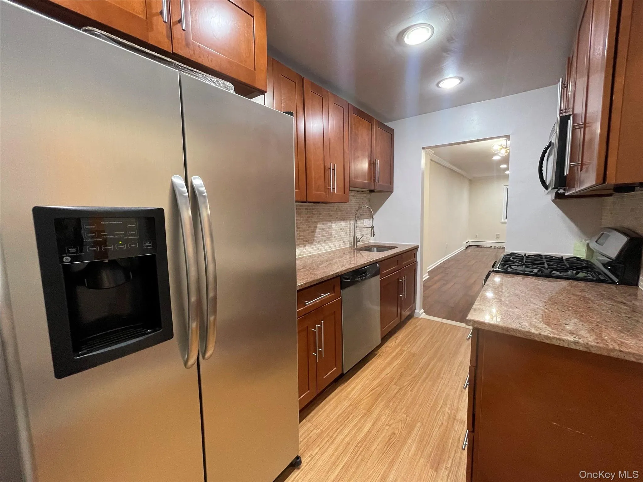 Kitchen featuring stainless steel appliances, light stone counters, light wood-type flooring, backsplash, and brown cabinets Kitchen featuring stainless steel appliances, light stone counters, light wood-type flooring, backsplash, and brown cabinets