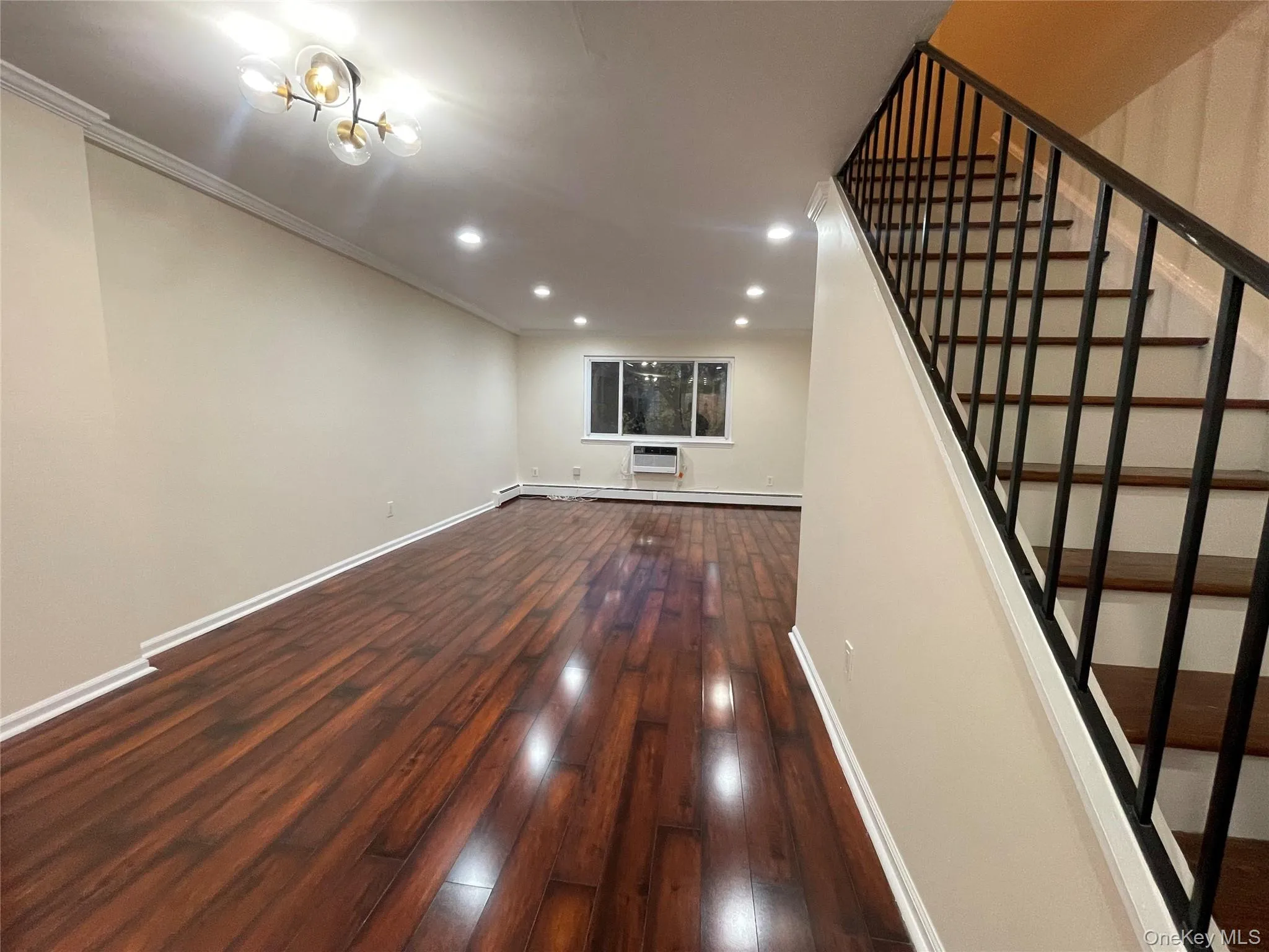 Unfurnished living room with dark wood-style flooring, recessed lighting, stairs, a baseboard heating unit, and crown molding Unfurnished living room with dark wood-style flooring, recessed lighting, stairs, a baseboard heating unit, and crown molding