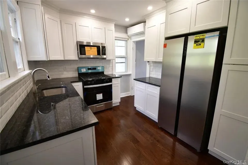 Kitchen with stainless steel appliances, white cabinetry, dark stone countertops, dark wood-style floors, and decorative backsplash Kitchen with stainless steel appliances, white cabinetry, dark stone countertops, dark wood-style floors, and decorative backsplash
