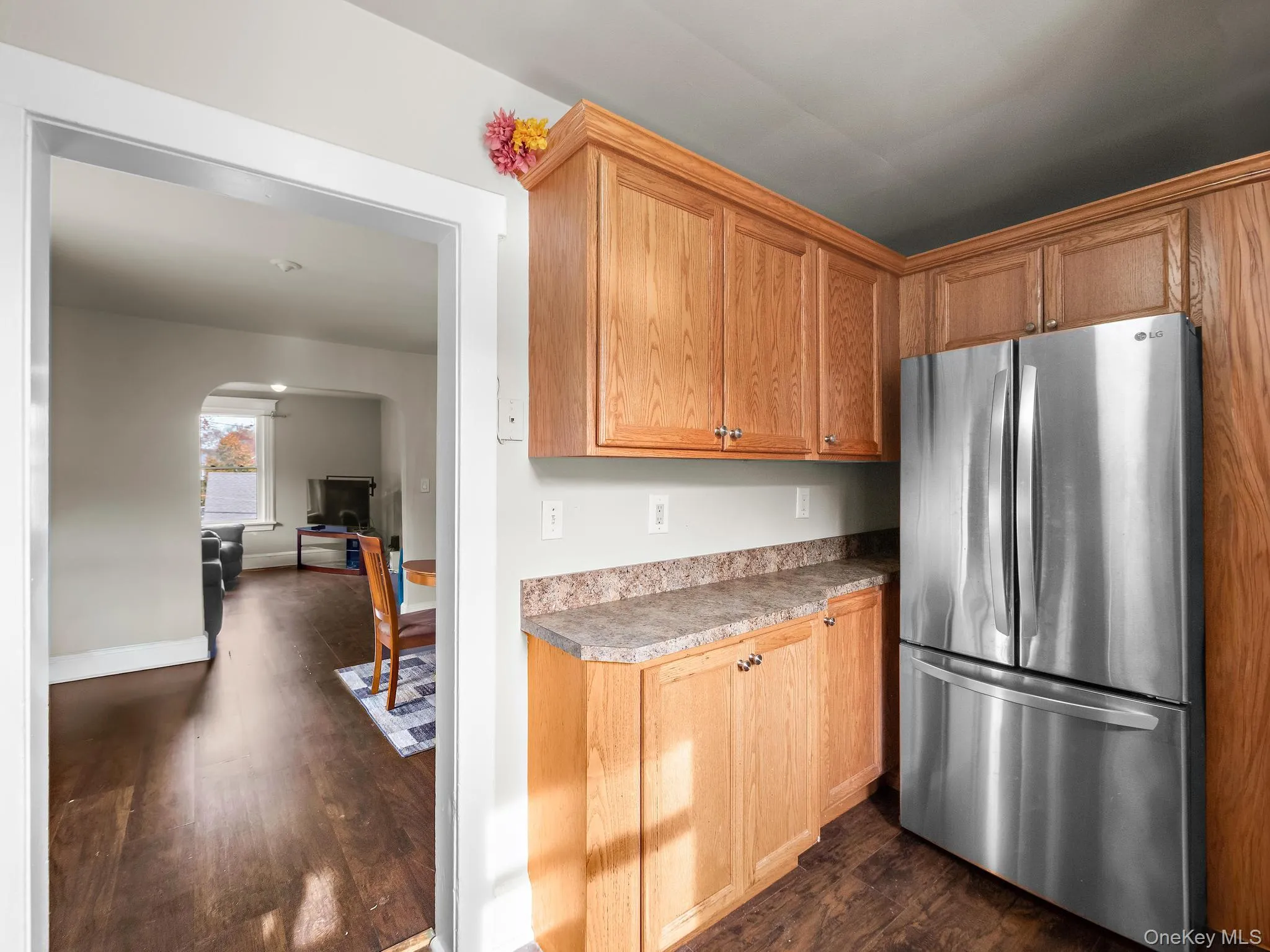 Kitchen featuring freestanding refrigerator, dark wood-style floors, arched walkways, light countertops, and brown cabinets Kitchen featuring freestanding refrigerator, dark wood-style floors, arched walkways, light countertops, and brown cabinets