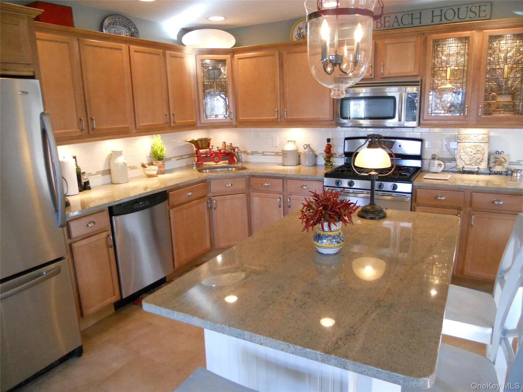 Kitchen featuring glass insert cabinets, appliances with stainless steel finishes, tasteful backsplash, light stone counters, and brown cabinets Kitchen featuring glass insert cabinets, appliances with stainless steel finishes, tasteful backsplash, light stone counters, and brown cabinets