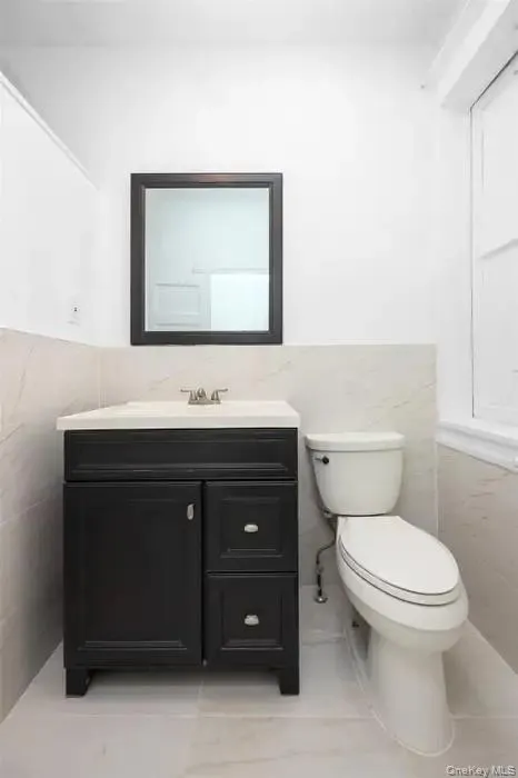Half bathroom with tile walls, a wainscoted wall, vanity, and light tile patterned flooring Half bathroom with tile walls, a wainscoted wall, vanity, and light tile patterned flooring