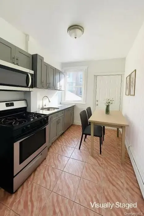 Kitchen with appliances with stainless steel finishes, gray cabinetry, light tile patterned floors, a baseboard radiator, and light countertops Kitchen with appliances with stainless steel finishes, gray cabinetry, light tile patterned floors, a baseboard radiator, and light countertops