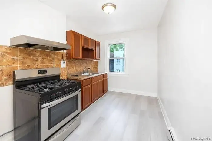 Kitchen with gas range, brown cabinets, decorative backsplash, custom range hood, and light wood finished floors Kitchen with gas range, brown cabinets, decorative backsplash, custom range hood, and light wood finished floors