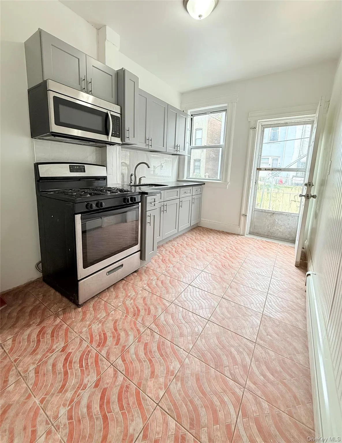 Kitchen featuring gray cabinetry, stainless steel appliances, light tile patterned floors, dark countertops, and backsplash Kitchen featuring gray cabinetry, stainless steel appliances, light tile patterned floors, dark countertops, and backsplash