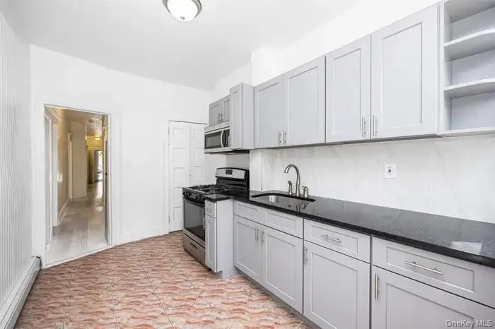 Kitchen with open shelves, stainless steel appliances, a baseboard heating unit, dark stone countertops, and gray cabinets Kitchen with open shelves, stainless steel appliances, a baseboard heating unit, dark stone countertops, and gray cabinets