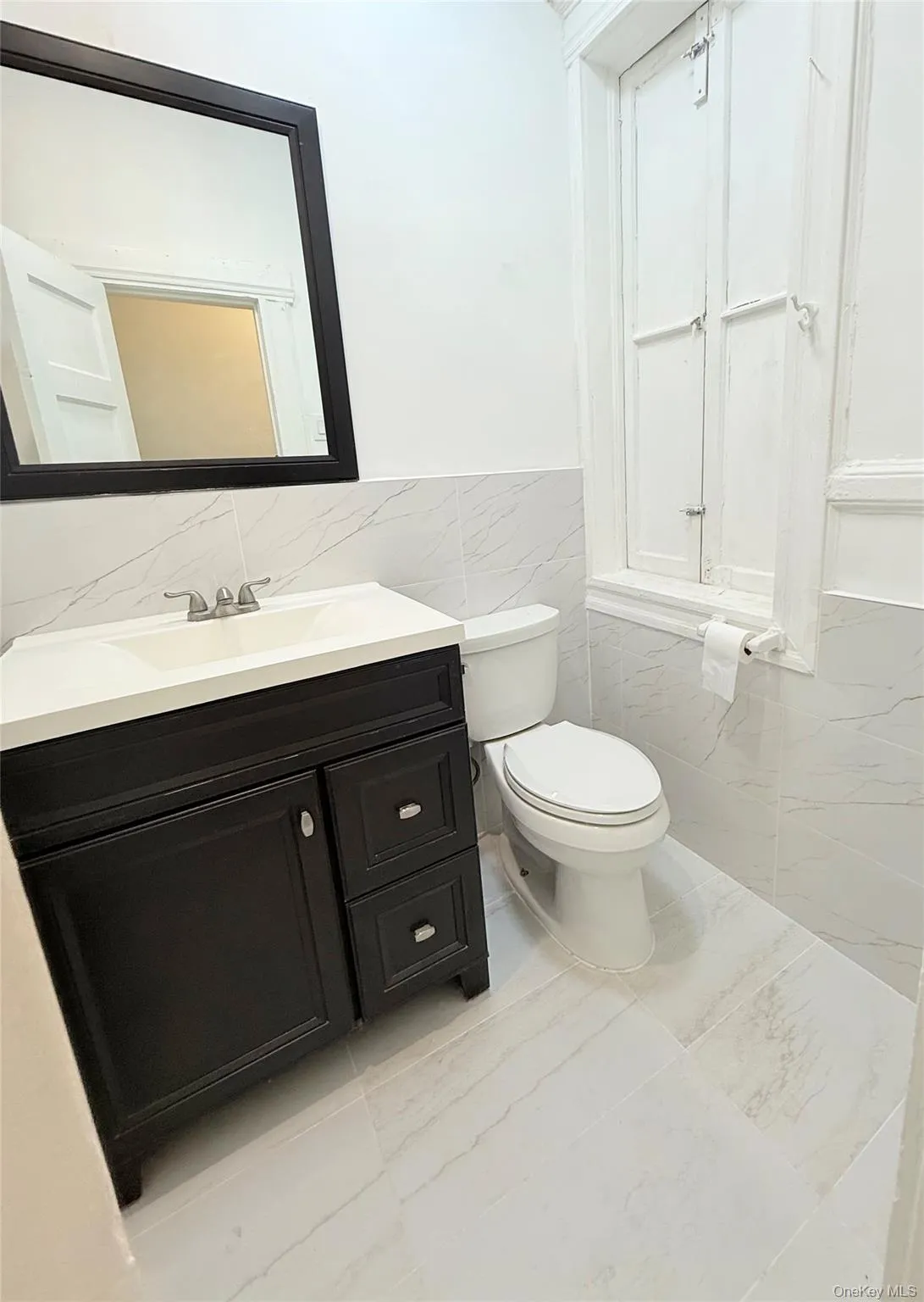 Half bath featuring tile walls, vanity, a wainscoted wall, and light tile patterned floors Half bath featuring tile walls, vanity, a wainscoted wall, and light tile patterned floors