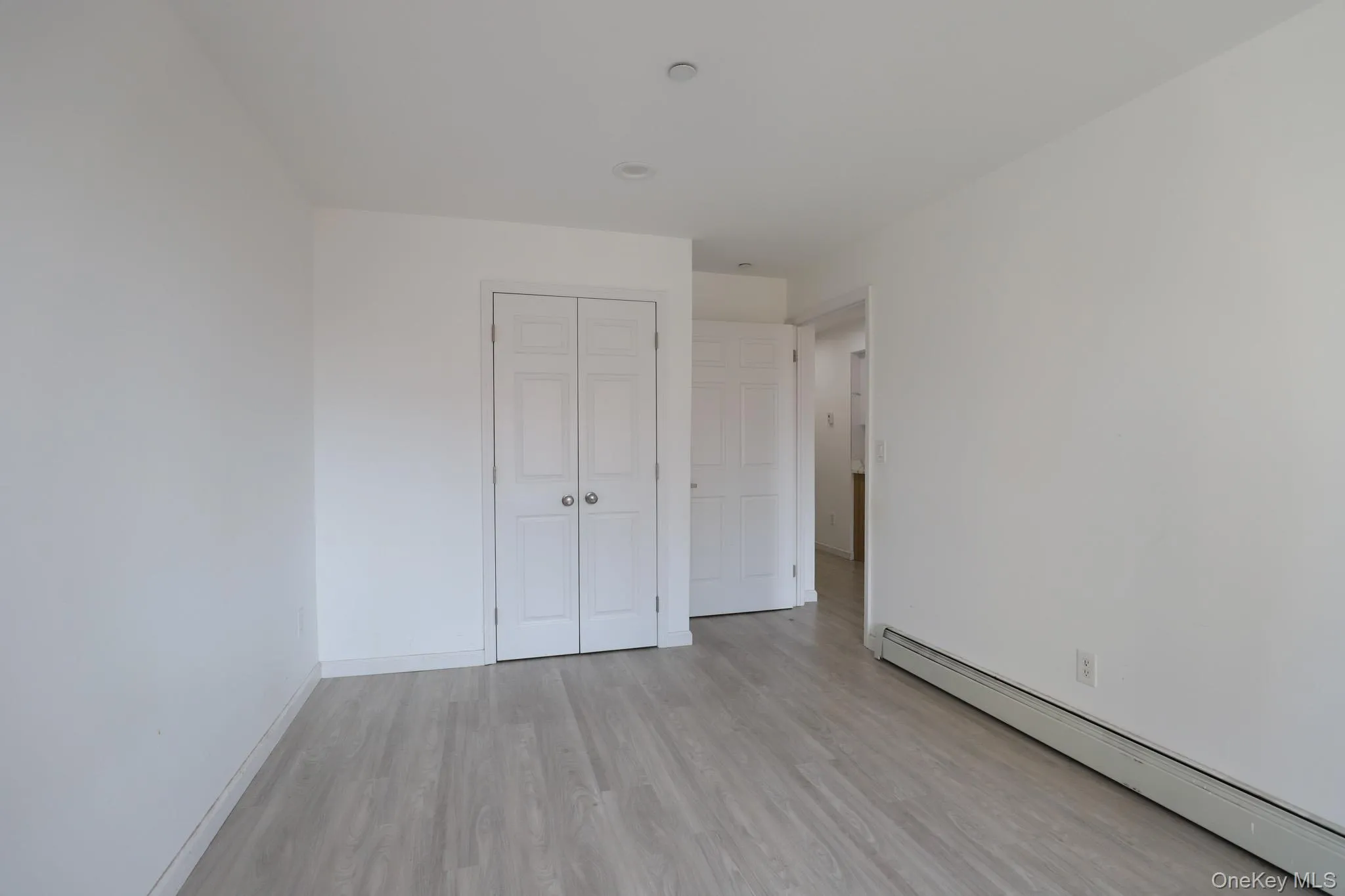 Unfurnished bedroom with a baseboard heating unit, light wood-style floors, and a closet Unfurnished bedroom with a baseboard heating unit, light wood-style floors, and a closet